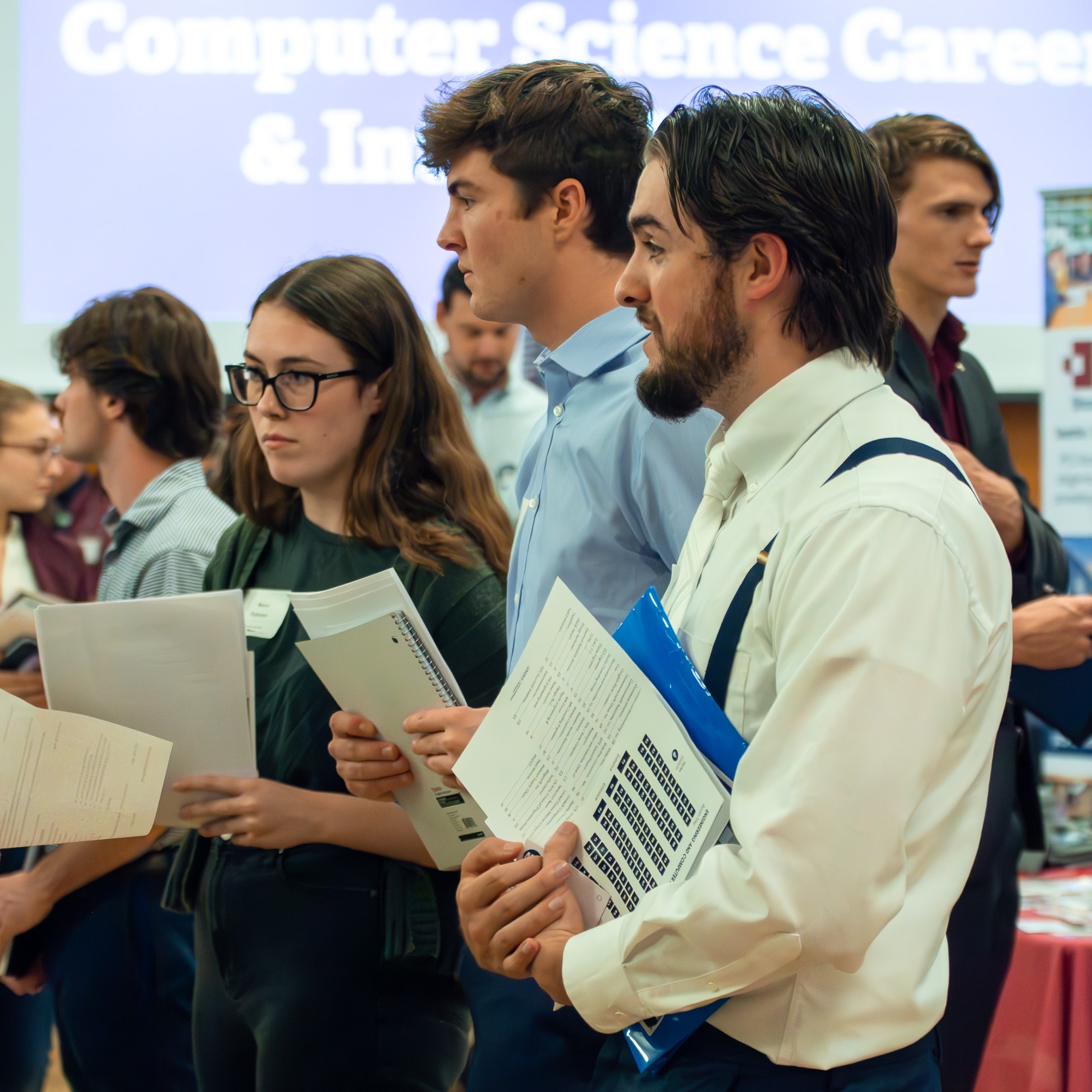 A line of students in professional attire stand in front of an employer at the Engineering and Computer Science Career and Internship Fair