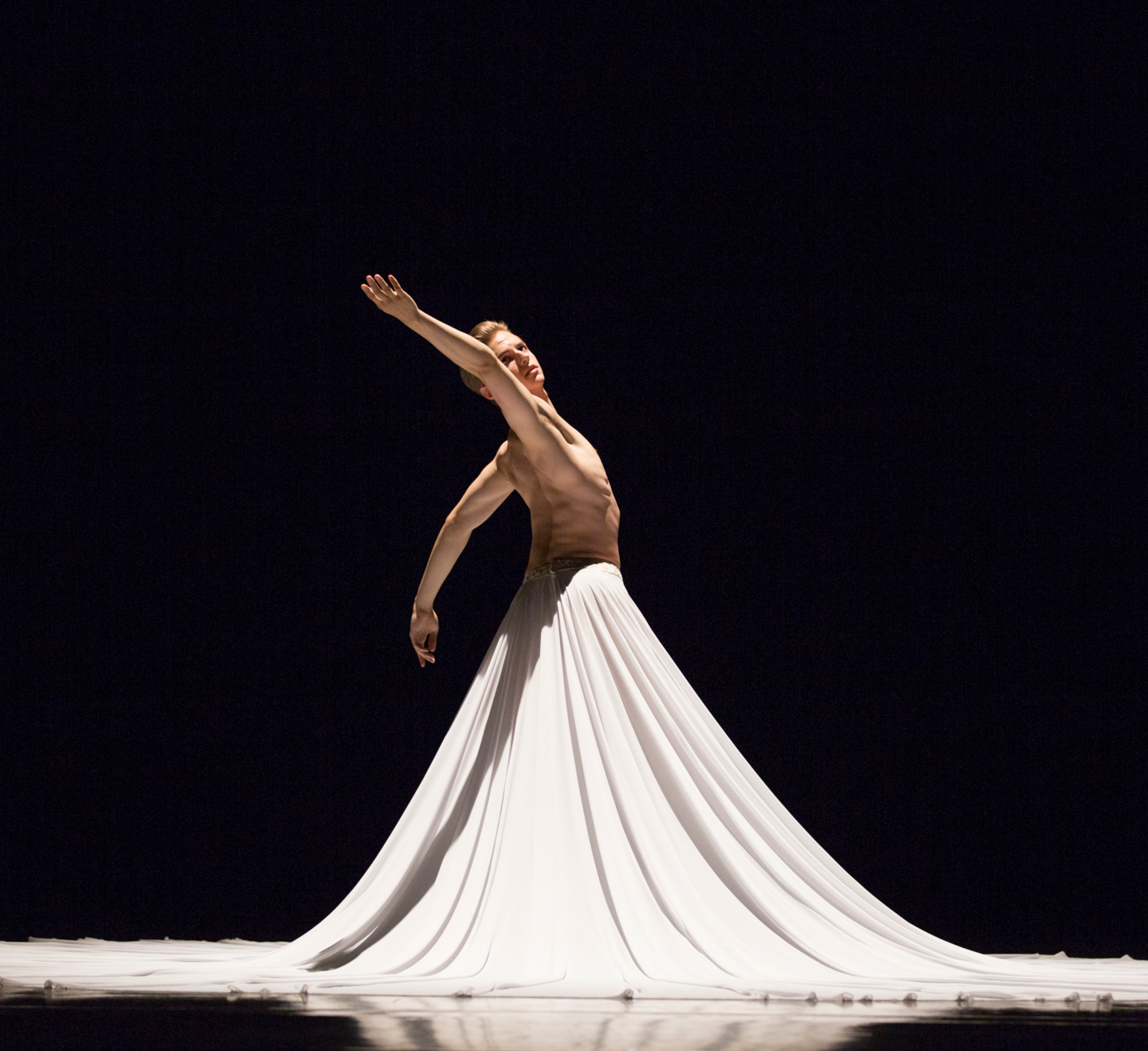 Ballet dancer against a black backdrop posing in a flowing white skirt.