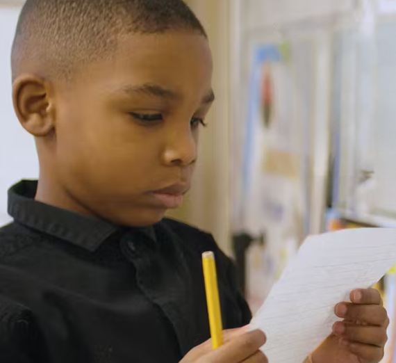 I little boy reading a piece of paper with a pencil in his hand. 