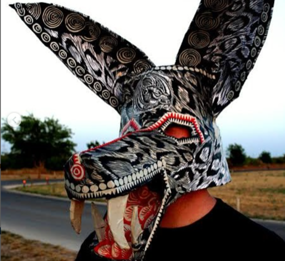 A person wearing a mask styled like a wold and bat with black and white designs and red accents.