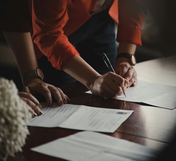 people writing on papers on a wood desk