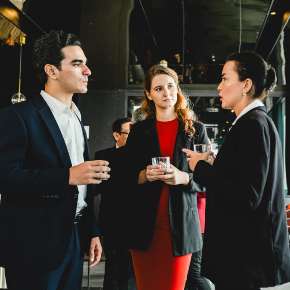 A group of three holds drinks and chats at a networking reception
