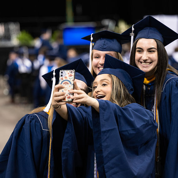 Four student huddle around a mobile phone for a selfie.