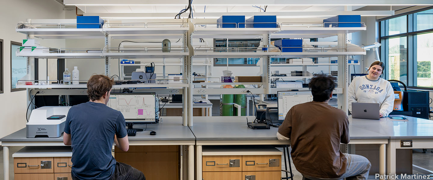 Three students at computer and equipment stations inside a clean lab 