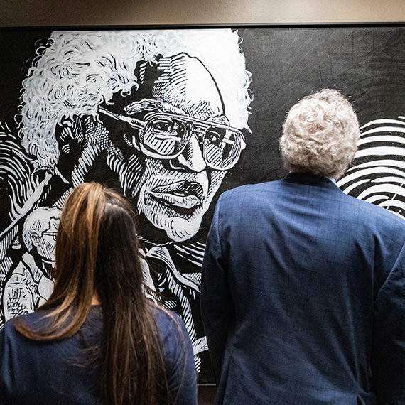 Two people view a portrait of Gonzaga Law alumni Carl Maxey