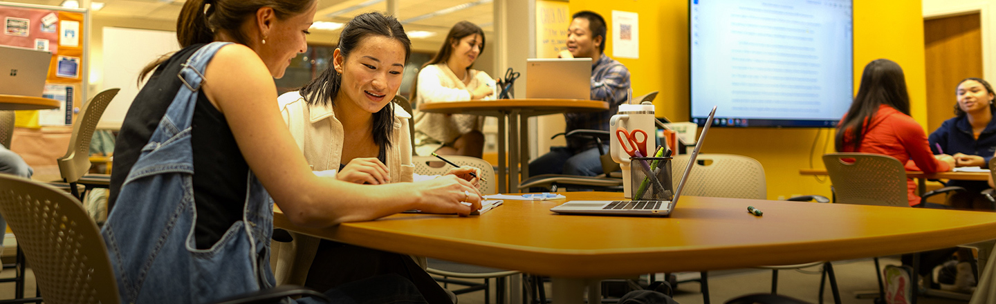Students looking at work on a table and talking together.