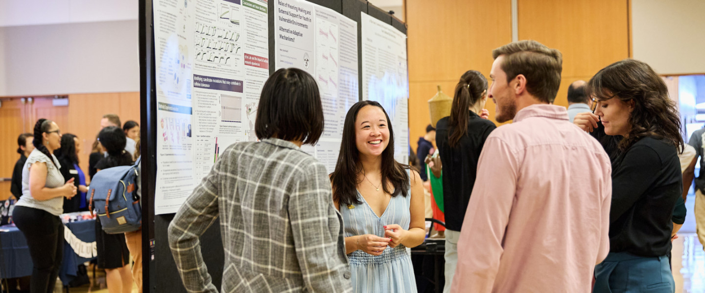 A student discussing their poster at a conference with a group of people.