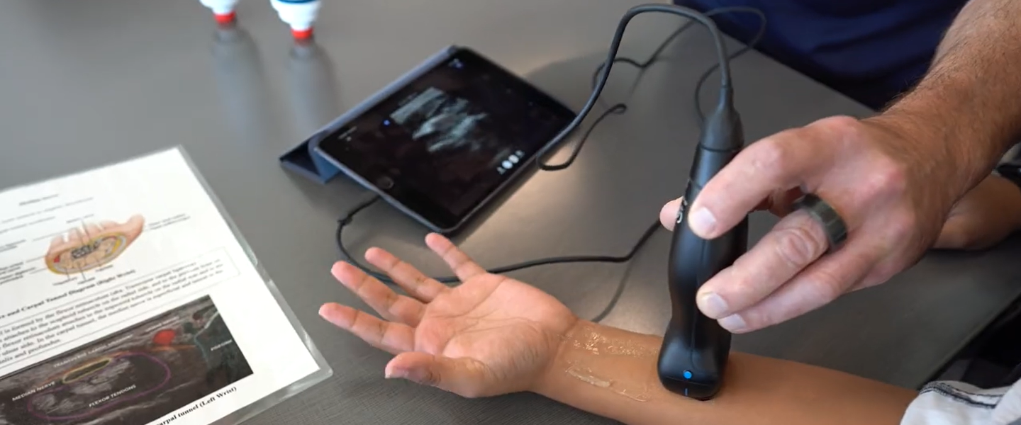 A professor applies an ultrasound device to a student's wrist