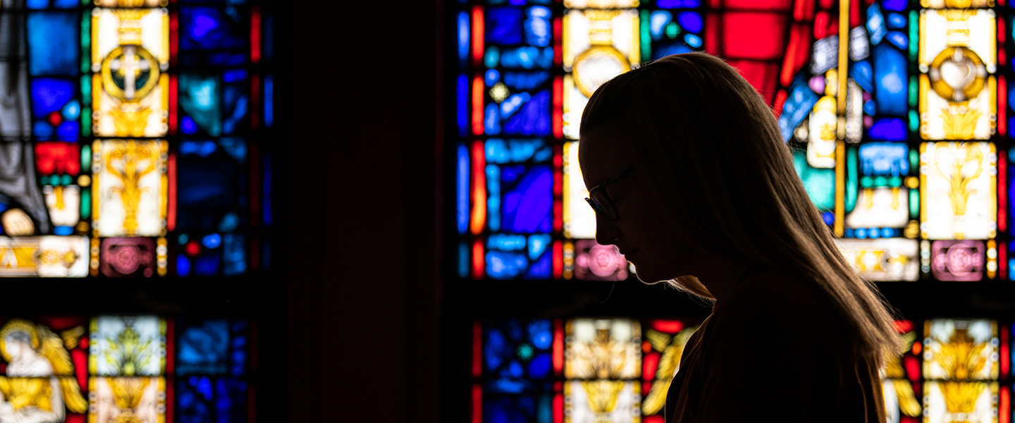 silhouette of person praying with stain glass background