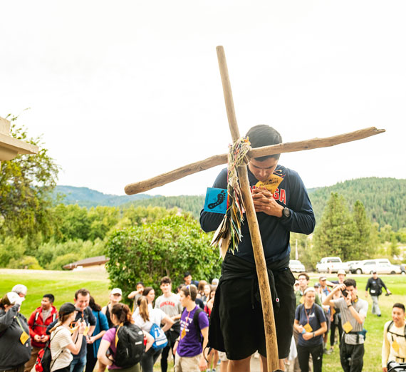 Student praying in front of a wooden cross at the Cataldo Mission in Idaho during Gonzaga University's annual Pilgrimage retreat