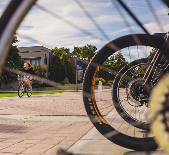 Student biking in the background of a bike wheel's spokes.