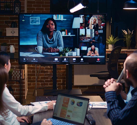Group of people in room at a table meeting with more people on a video conference call