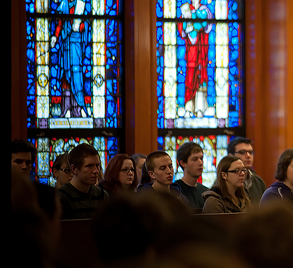 Students listen to a lecture. Stained glass is the background.