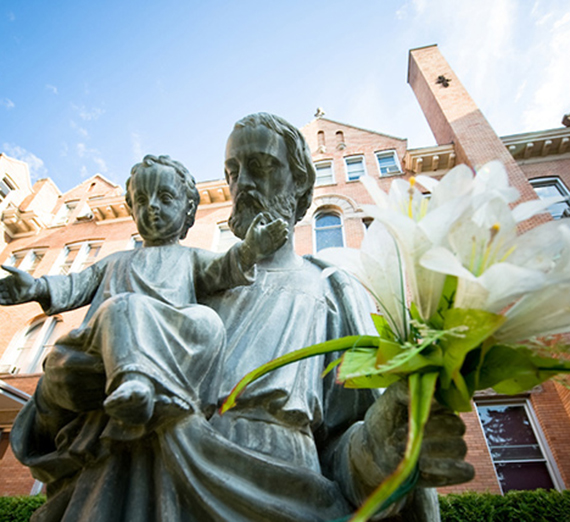 The Statue of St. Joseph holding an infant Jesus Christ in the foreground of College Hall.