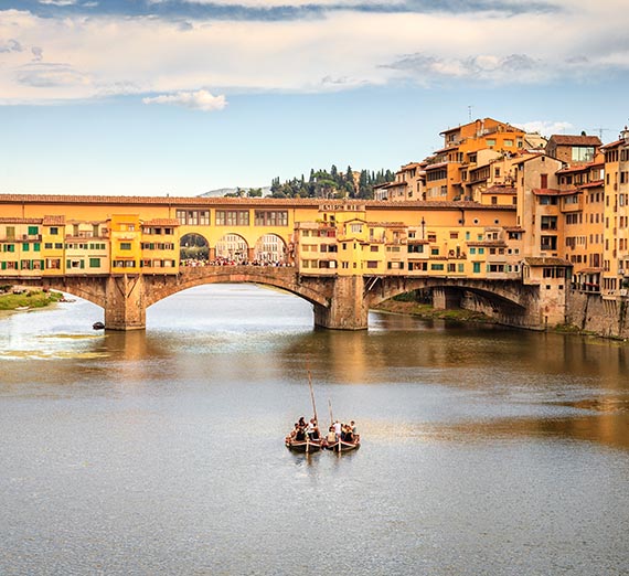 A river with two boats in front of a bridge at Ponte Vecchio, Florence