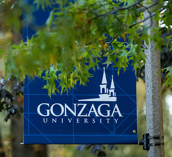 A blue Gonzaga post banner behind green tree leaves