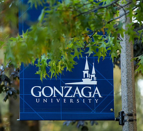 A blue Gonzaga post banner behind green tree leaves