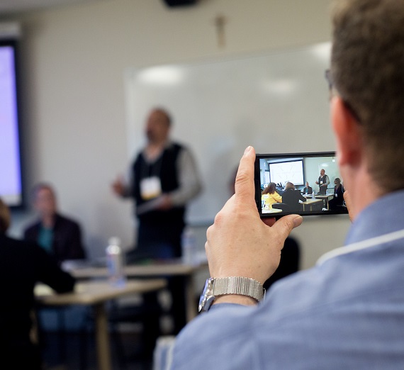 An audience member takes a photo with a smartphone during a presentation. 