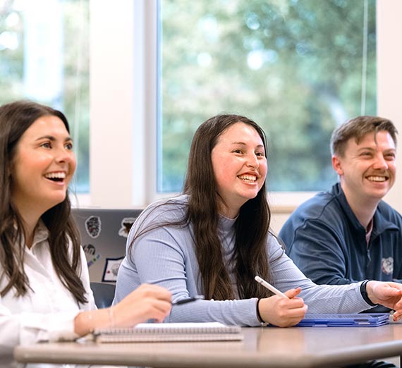 Graduate Accounting Students Smiling at Desks in Class