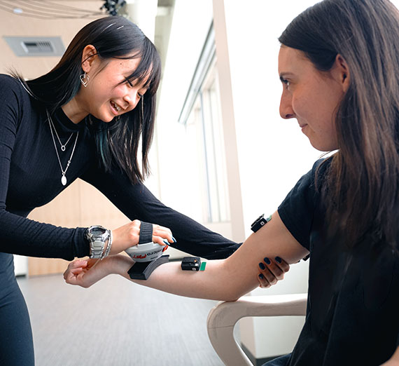 woman applies medical device to another woman's arm