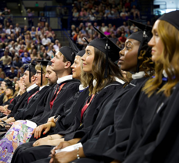 Graduates sit at commencement while listening to speaker