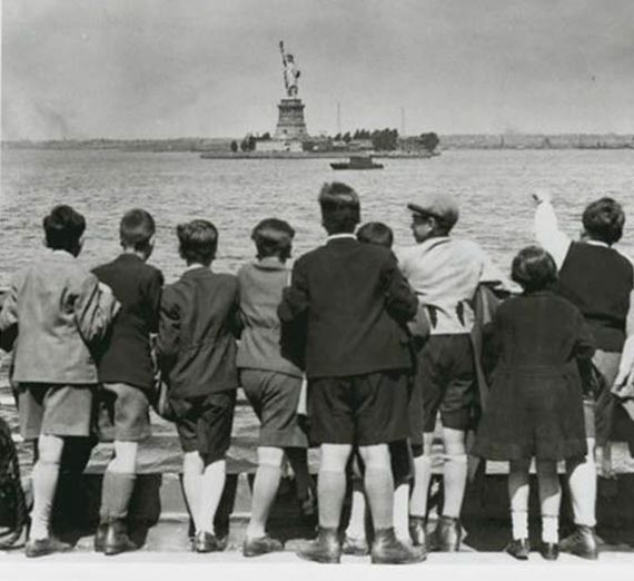 Black and white photo of a group of young boys looking at Ellis Island and the Statue of Liberty.