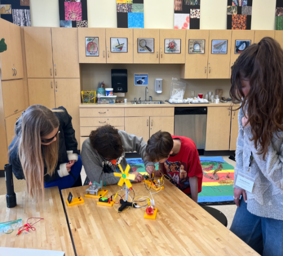 kids learning at a table in a classroom with teacher standing nearby