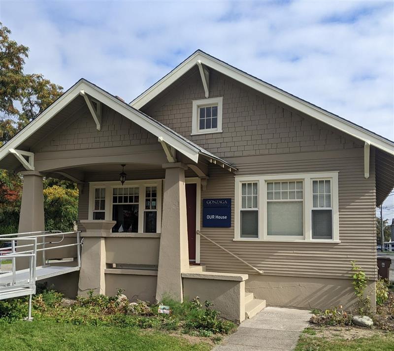 The image depicts the front of OUR House which is a gray one story house with white trim and steps up to a red door. 