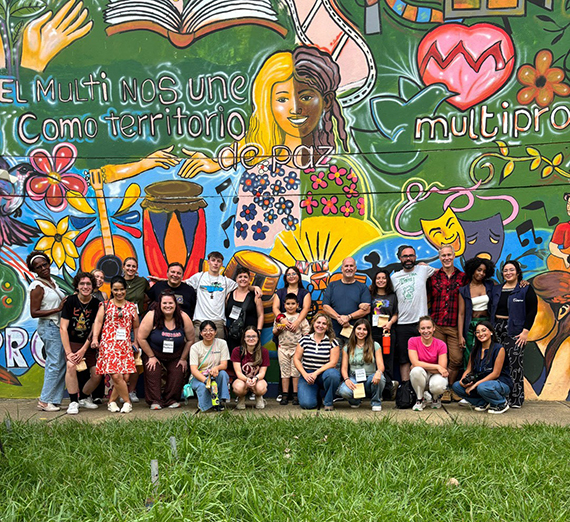 Group of 23 people standing in front of a painted wall.