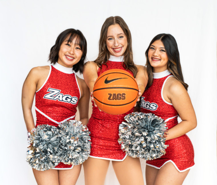 Three dancers holding poms and a basketball