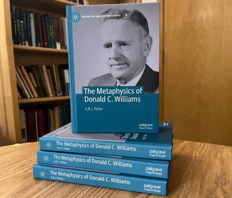 A stack of books on a table titled "The Metaphysics of Donald C. Williams" written by A.R.J. Fisher 