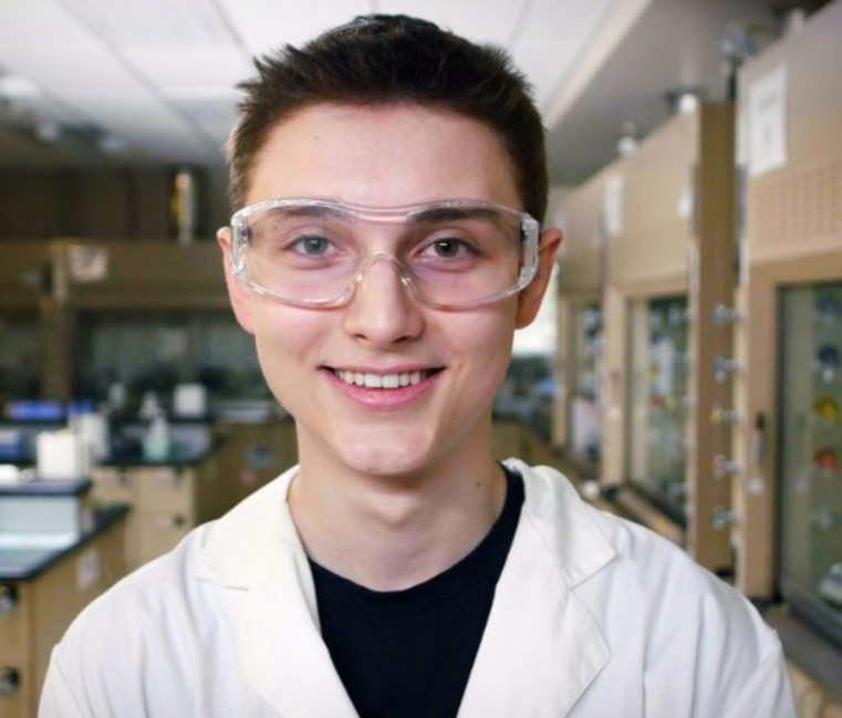 A student wearing goggles and a lab coat. 