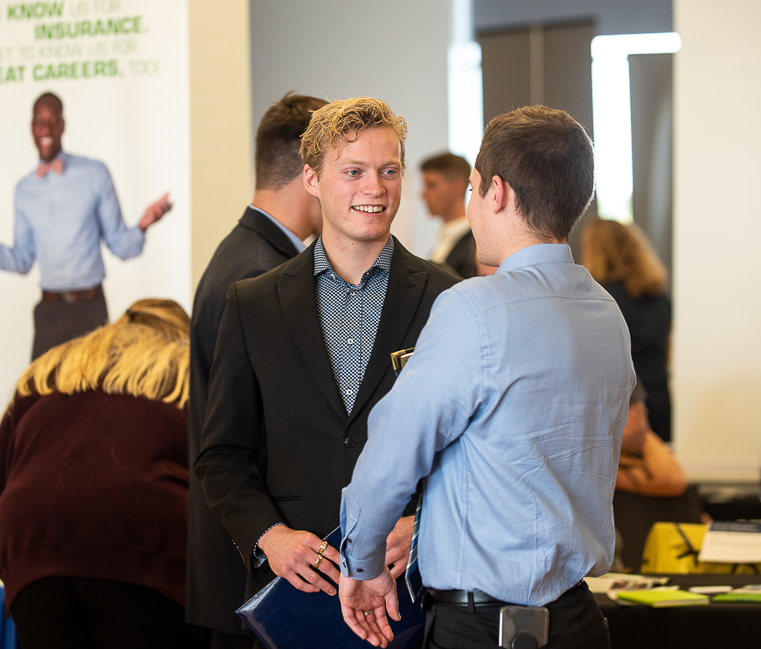 Two male students stand together in front of an employer booth at the All Majors Career and Internship Fair.