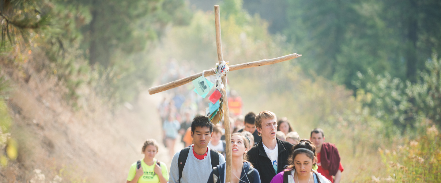 Students walk in a line behind the leader carrying a cross