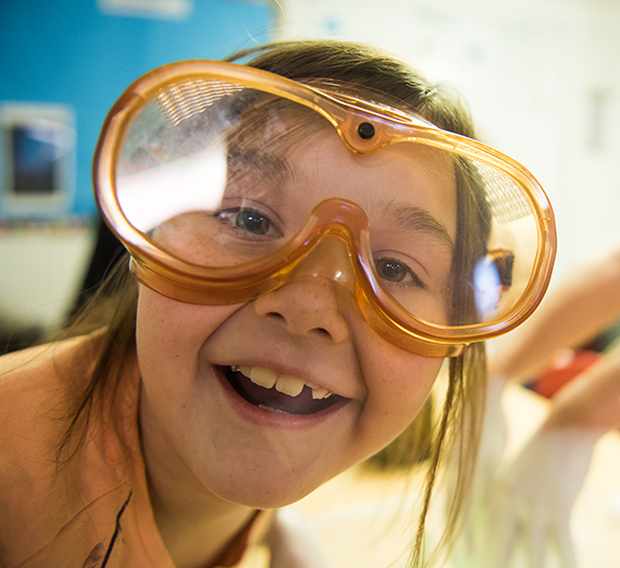 A child wearing safety goggles smiles into the camera