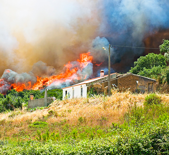 A wildfire rages behind a home near a wooded area