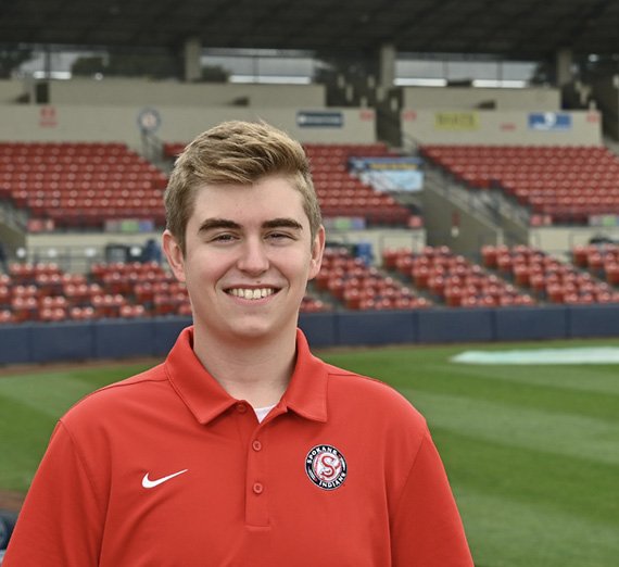 Cody Wright standing in a baseball stadium with a red polo on. 