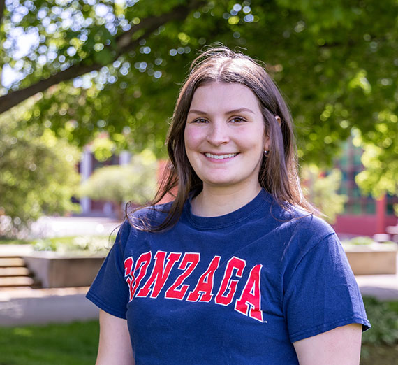 Steph McLaren, female wearing blue tshirt with "Gonzaga" in red writing, trees and campus in background
