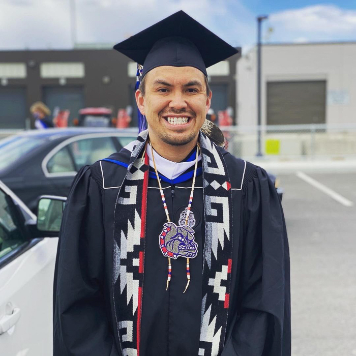 James smiles proudly in his black graduation cap and gown, a stole with traditional designs worn in place of the white one. 