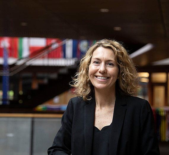Woman in black blazer and black shirt with building interior in background. 