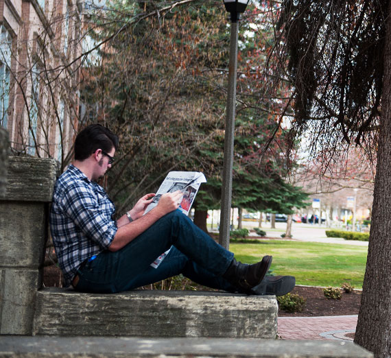 Student reading a newspaper on the steps of College Hall