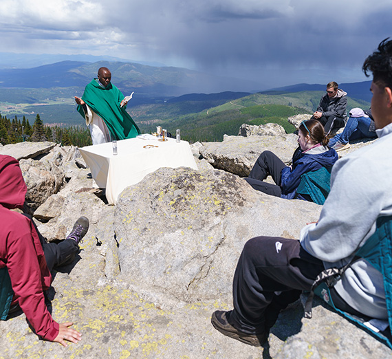 A pastor leads worship service outoors at the top of a rocky mountain.