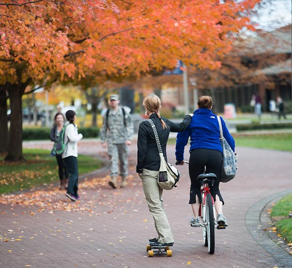 Women biking and skateboarding on campus.
