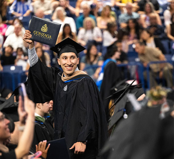 Smiling Graduate student raises diploma folder updward.