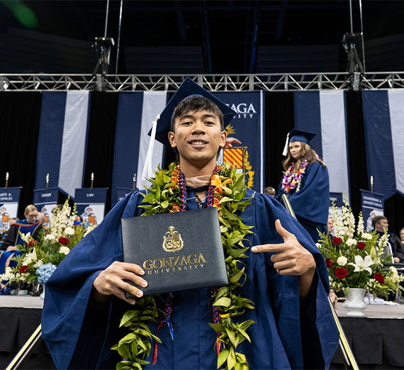 Granduating student smiles and points at diploma folder.