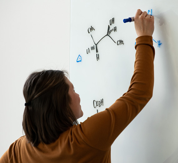 A professor draws a chemistry equation on the whiteboard in The Bollier Center.