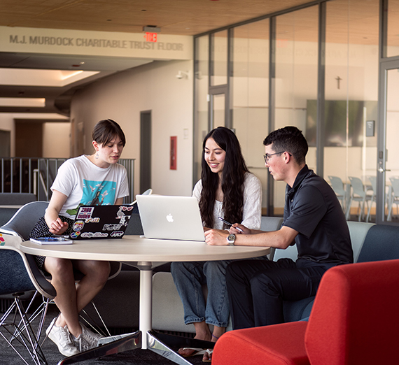 Three student gather around a laptop computer.