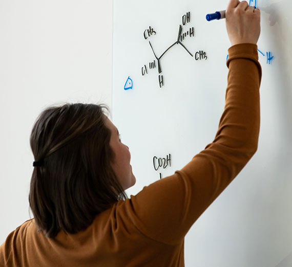 A professor draws a chemistry equation on the board.
