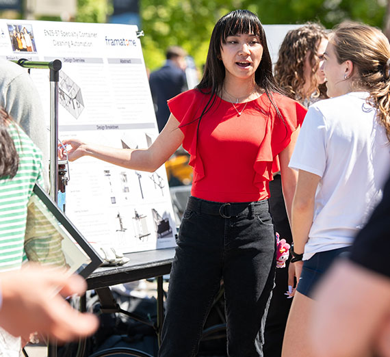 woman points to an academic poster talking with another person outside on a sunny day