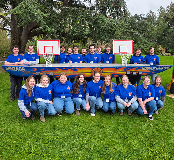 More than a dozen students pose around a long canoe made of concrete decorated with a basketball theme